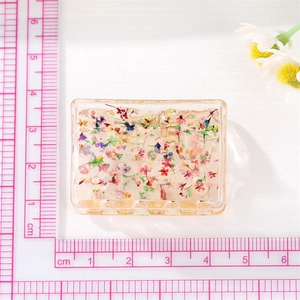 Pince à cheveux rectangulaire en résine avec fleurs séchées à côté d'une règle rose