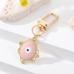 Llavero de ojo turco rosa con marco dorado y detalles florales sobre piedra blanca