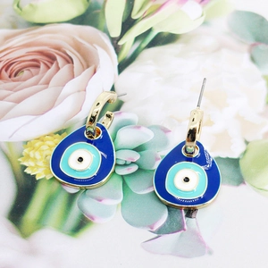 Close-up of golden Evil Eye drop earrings with deep blue enamel and teardrop design