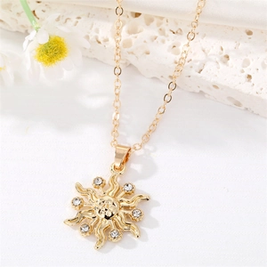 Collana con ciondolo a sole dorato retrò e zirconi lucenti su sfondo di pietra bianca