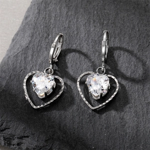 Sparkling silver heart pendant earrings with clear zircon on a dark textured stone surface
