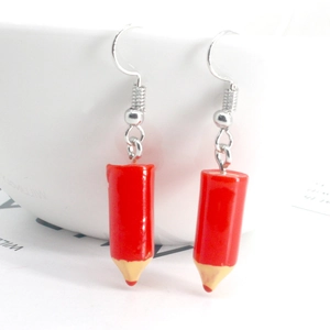 Detailed view of red pencil-shaped resin earrings hanging on a white bowl rim