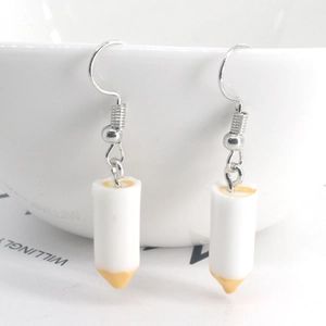 Close-up of white resin pencil-shaped earrings hanging on a white ceramic bowl