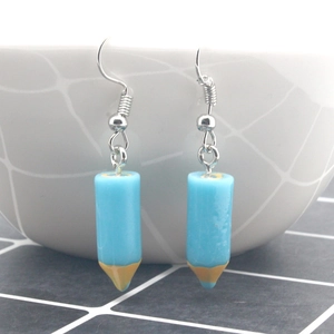 Detailed close-up of creative blue pencil resin earrings with metal hooks on a white grid
