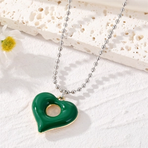 Deep green heart cutout necklace with gold trim on a silver bead chain shown on white stone