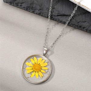 Macro detail of round resin pendant with yellow daisy flower and silver flakes