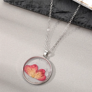 Macro detail of round pendant with real red dried flowers and silver flakes inside