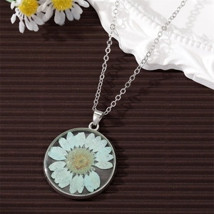 Macro detail of a clear round pendant with a real light blue dried flower on a silver chain