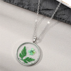 Close-up of round silver necklace with dried green flower and silver leaf flakes inside