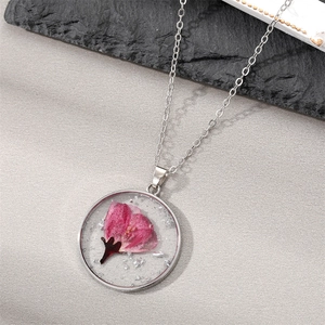 Detailed macro view of a round resin necklace pendant with real pink dried flowers