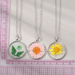 Three variants of real dried flower glass pendants with silver flakes and a scale reference