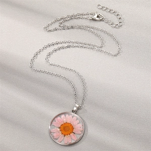 Detail of silver pendant necklace featuring a pink dried daisy flower set in a round charm