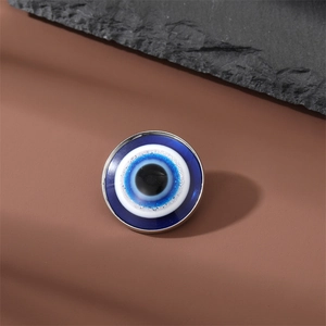 Macro shot of silver-framed evil eye charm with blue enamel layers on a stone background