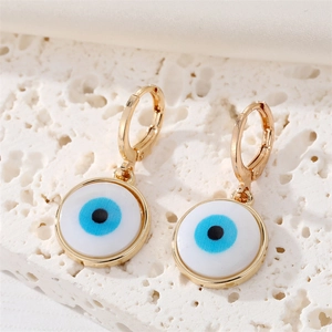 Close-up of bohemian golden evil eye hoop earrings on white stone and silk background