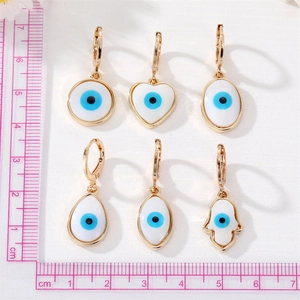 Detail view of six gold evil eye hoop earrings with hamsa and heart charms on a scale