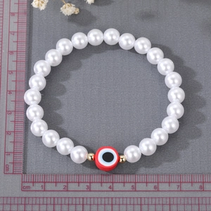Detailed macro view of white pearl bracelet featuring a red evil eye charm and gold beads