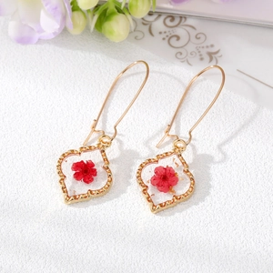 Vue détaillée de boucles d'oreilles cœur dorées avec fleurs séchées rouges et feuilles d'or