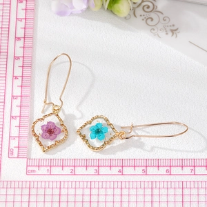 Détail de boucles d'oreilles dorées de 6cm avec de vraies fleurs séchées et résine