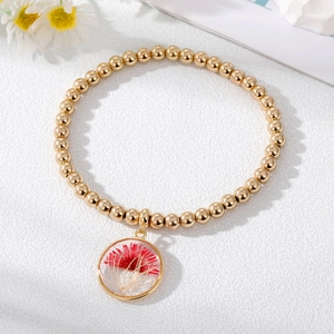 Bracciale a sfere dorate con ciondolo in vetro e margherita rossa essiccata su fondo bianco