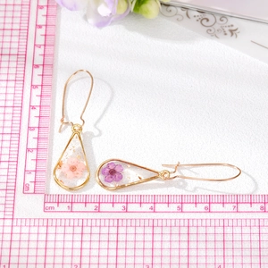 Detailed close-up of handmade water-drop resin earrings with real pink and purple dried flowers