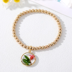 Dettaglio del bracciale con perline dorate e ciondolo con veri fiori secchi rossi