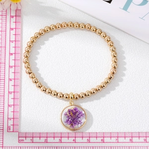 Dettaglio del bracciale con perline dorate con ciondolo di fiori secchi viola e misure