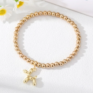 Fashionable gold beaded bracelet with a creative balloon dog charm on a stone background