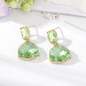 Detail view of gold-tone geometric earrings featuring faceted green crystals on white surface