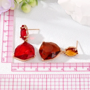 Macro shot of fan-shaped crystal earrings with red and amber stones in gold finish