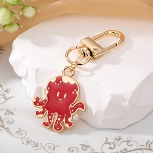 Cute red octopus metal keychain with gold finish and smiling face on white marble stone
