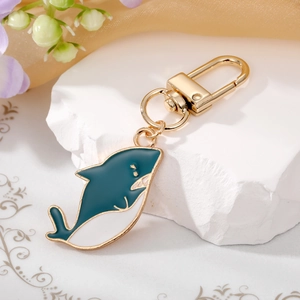 Detail of shark-shaped green enamel keychain with gold metal plating on marble