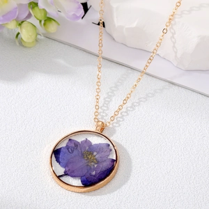 Détail d'un collier pendentif rond doré avec véritable fleur séchée mauve sur pierre