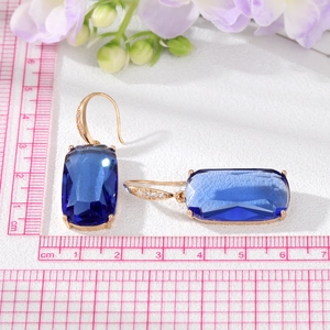 Détail de boucles d'oreilles dorées avec grands cristaux bleus et petits zircons blancs