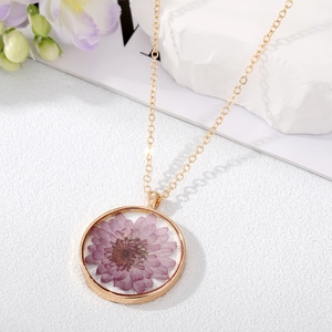 Vue détaillée d'un pendentif rond doré orné de fleurs séchées violettes