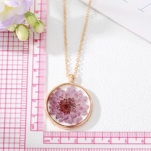 Détail du collier rond doré avec fleurs séchées violettes et une règle de mesure