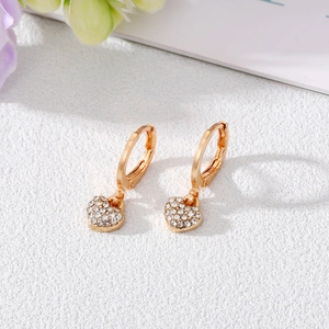 Sparkling gold heart drop earrings with white crystals on a rustic stone surface