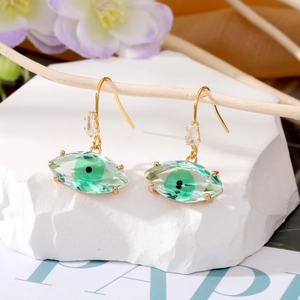 Pendientes de Ojo Turco con cristales verdes y acabado dorado sobre roca blanca