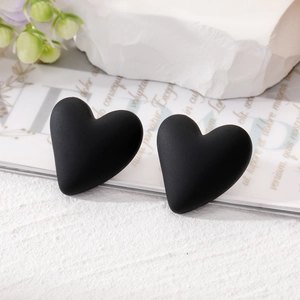 Elegant matte black heart-shaped stud earrings displayed on a white decorative stone base