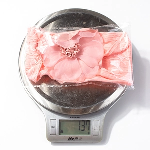 Bandeau bébé rose avec fleur pesant 13,7g sur une balance électronique pour détails de poids
