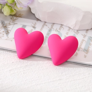 Close-up of bright pink matte heart earrings on a stylish magazine and stone background