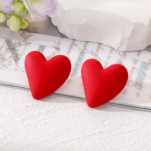 Close-up of heart-shaped matte red earrings on a stylish white textured background