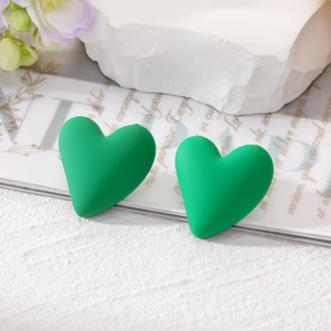 Close-up of matte green heart stud earrings on white marble and magazine background