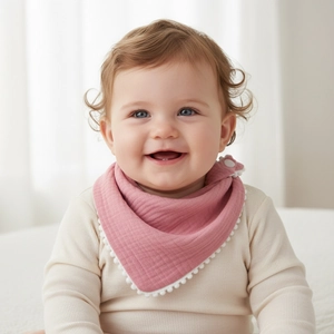 Detail of soft muslin baby bib in dusty pink with white pom-pom trim and snap closure