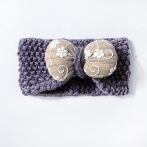 Detail of purple knitted baby headband with cream embroidered bow and floral motifs