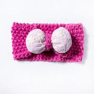 Detail of baby knitted headband featuring rose pink yarn and purple bow with white flower embroidery