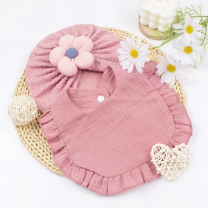 Set bavaglino rosa con volant e cappellino floreale per neonato su sfondo intrecciato