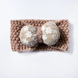 Detailed knit texture of khaki winter headband featuring a white floral bow embroidery