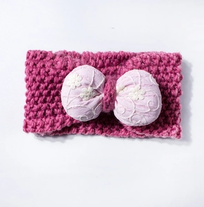 Détail d'un bandeau tricoté pour bébé en laine rose avec un nœud rose brodé de fleurs