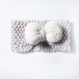 Detail of baby knitted headband featuring cream wool texture and embroidered bow design