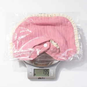 Pink cotton baby bib with lace trim being weighed at 19.5g for lightweight comfort